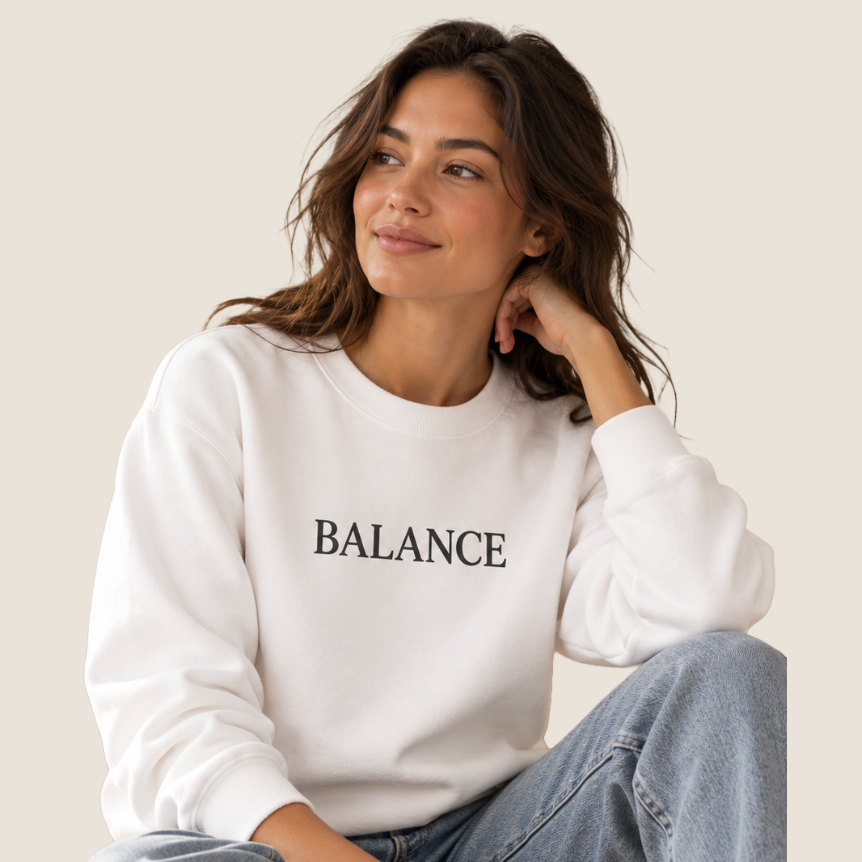 Woman wearing a white crewneck sweatshirt with "BALANCE" across the chest.