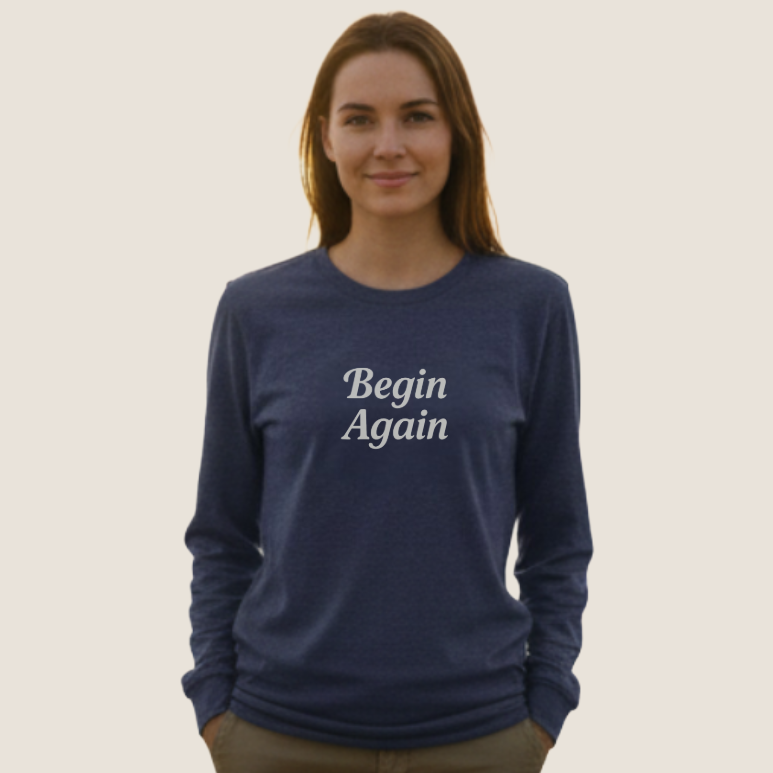 A woman wearing a navy blue long-sleeve crewneck sweatshirt with 'Begin Again' printed in white script on the chest.