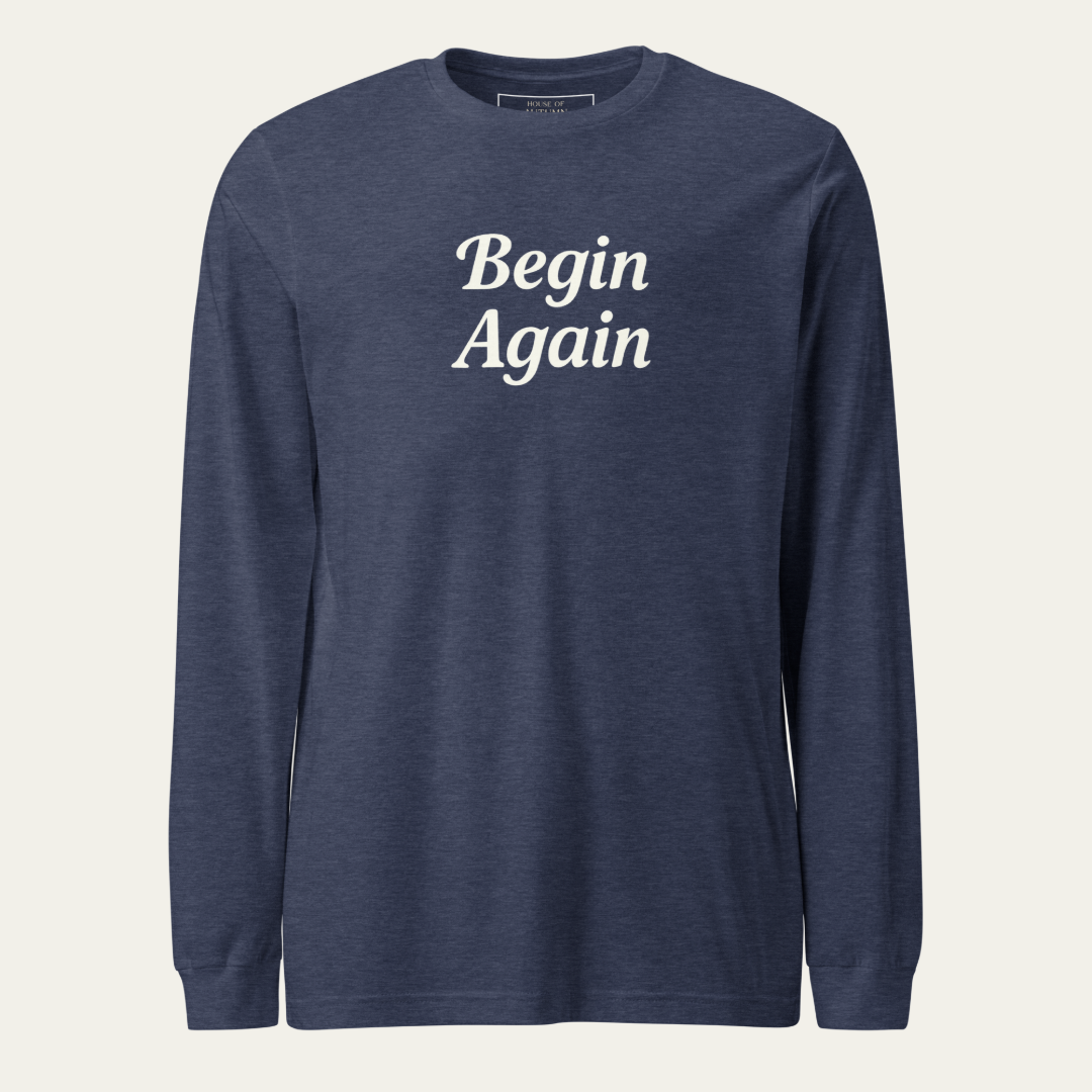 A navy blue long-sleeve crewneck shirt with the words 'Begin Again' printed in white serif text across the chest, displayed on a clean off-white background.