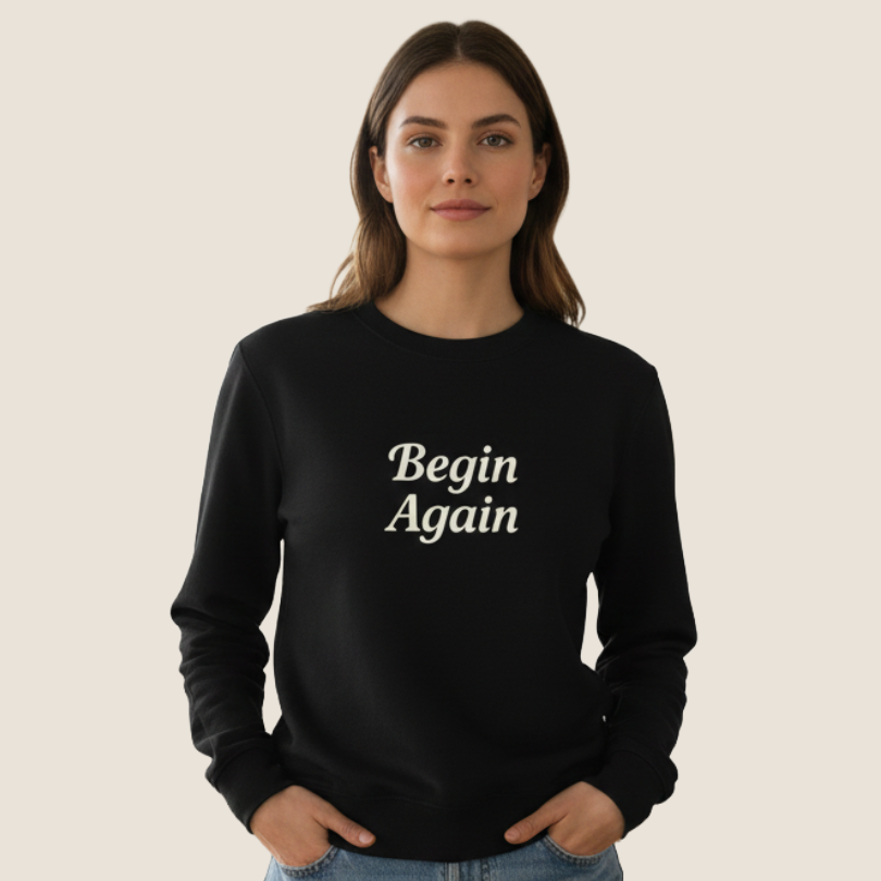 Woman wearing a black sweatshirt with "Begin Again" on the front.