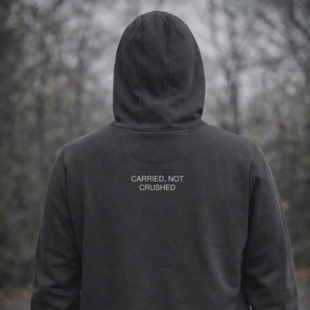 Person wearing a dark hoodie with 'CARRIED, NOT CRUSHED' text in a forest setting
