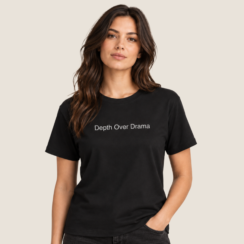 A woman modeling a black short-sleeve crewneck t-shirt with the phrase 'Depth Over Drama' printed in white across the chest, set against a solid light beige background.