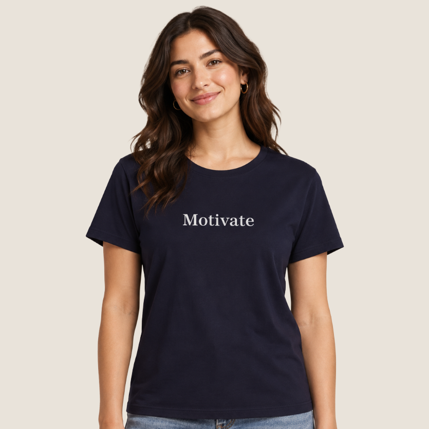 A woman modeling a navy blue short-sleeve t-shirt with the word 'Motivate' printed in white serif font across the chest, paired with light-wash blue jeans against a solid light beige background.