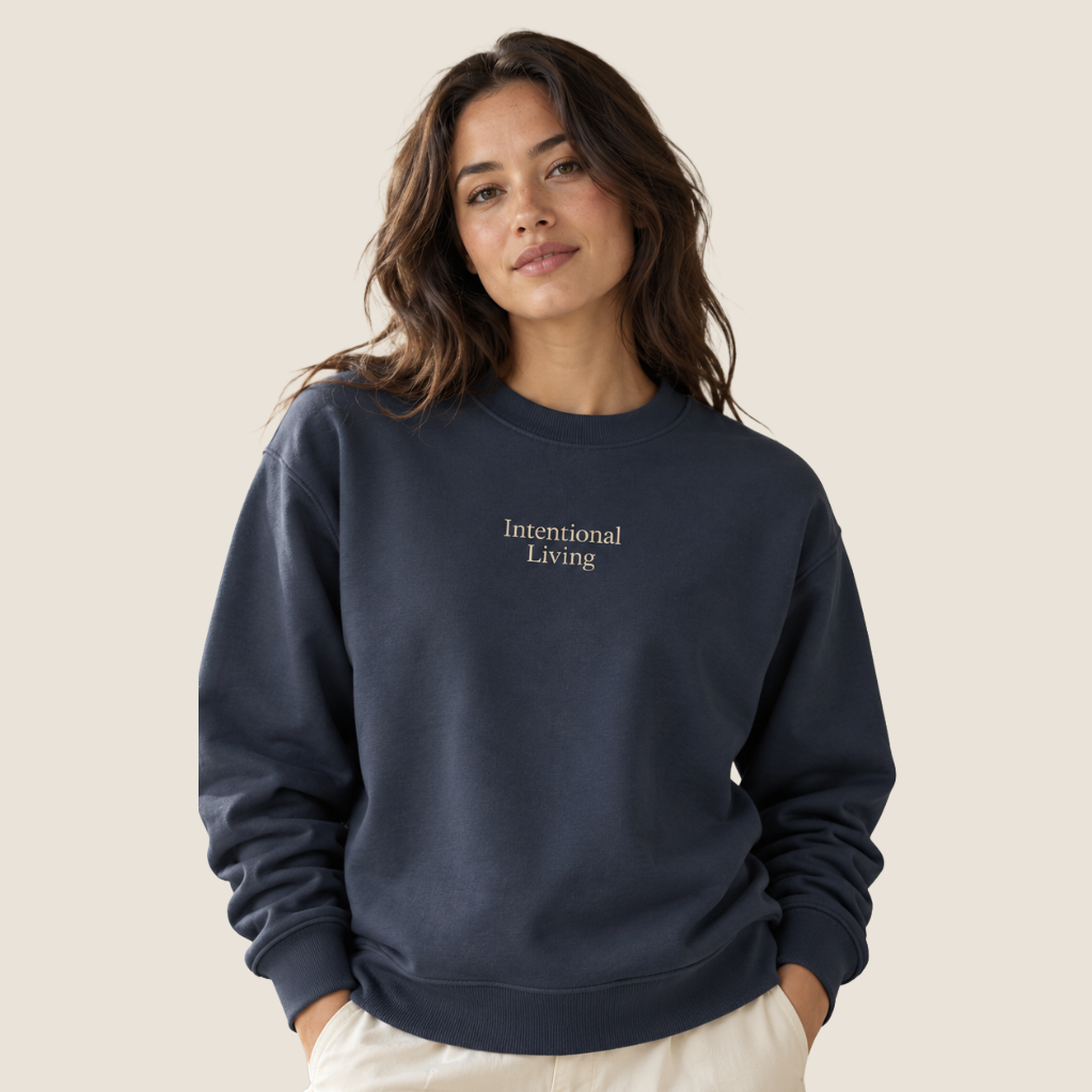 Woman wearing a navy crewneck sweatshirt that has "Intentional Living" on the center chest.
