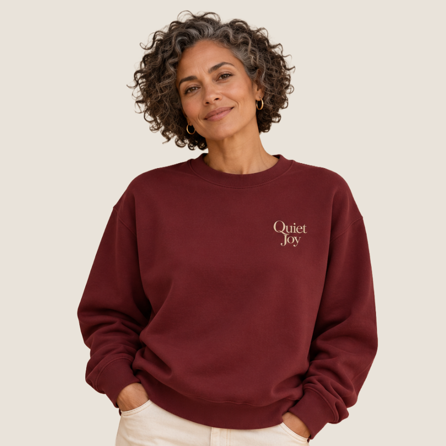 Woman wearing a maroon sweatshirt with Quiet Joy on the upper left chest.