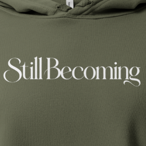 Still Becoming text on an olive green cropped hoodie