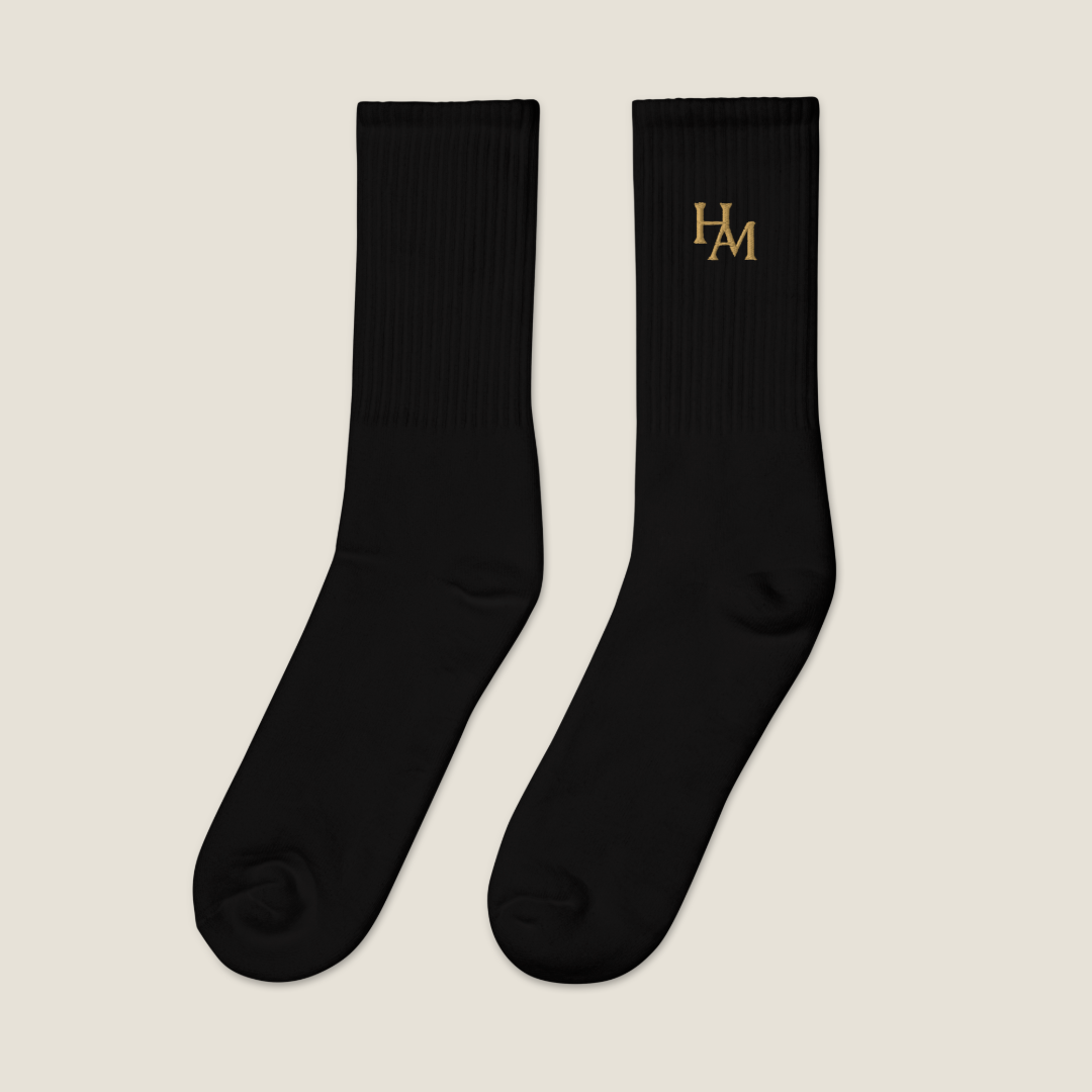 A pair of black crew socks with the brand name 'HAM' embroidered in gold on the upper calf, displayed against a solid white background.