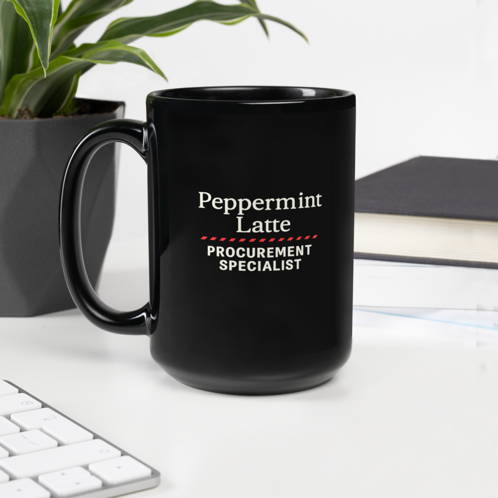 Black mug with 'Peppermint Latte Procurement Specialist' text on a desk with a plant and notebook in the background.