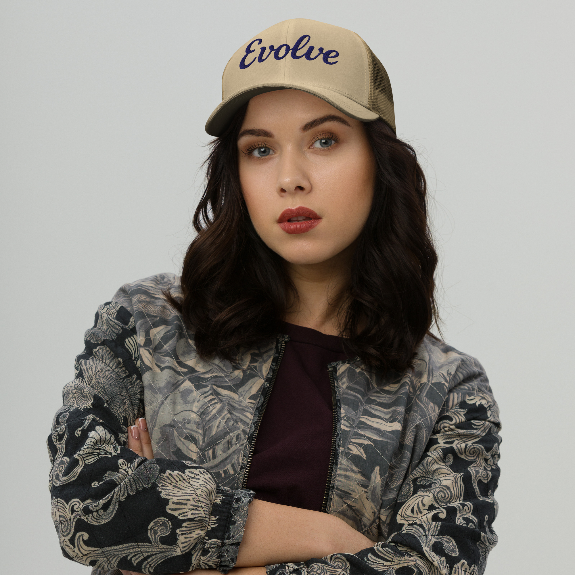 Woman wearing a beige cap with 'Evolve' text and a patterned jacket on a plain background