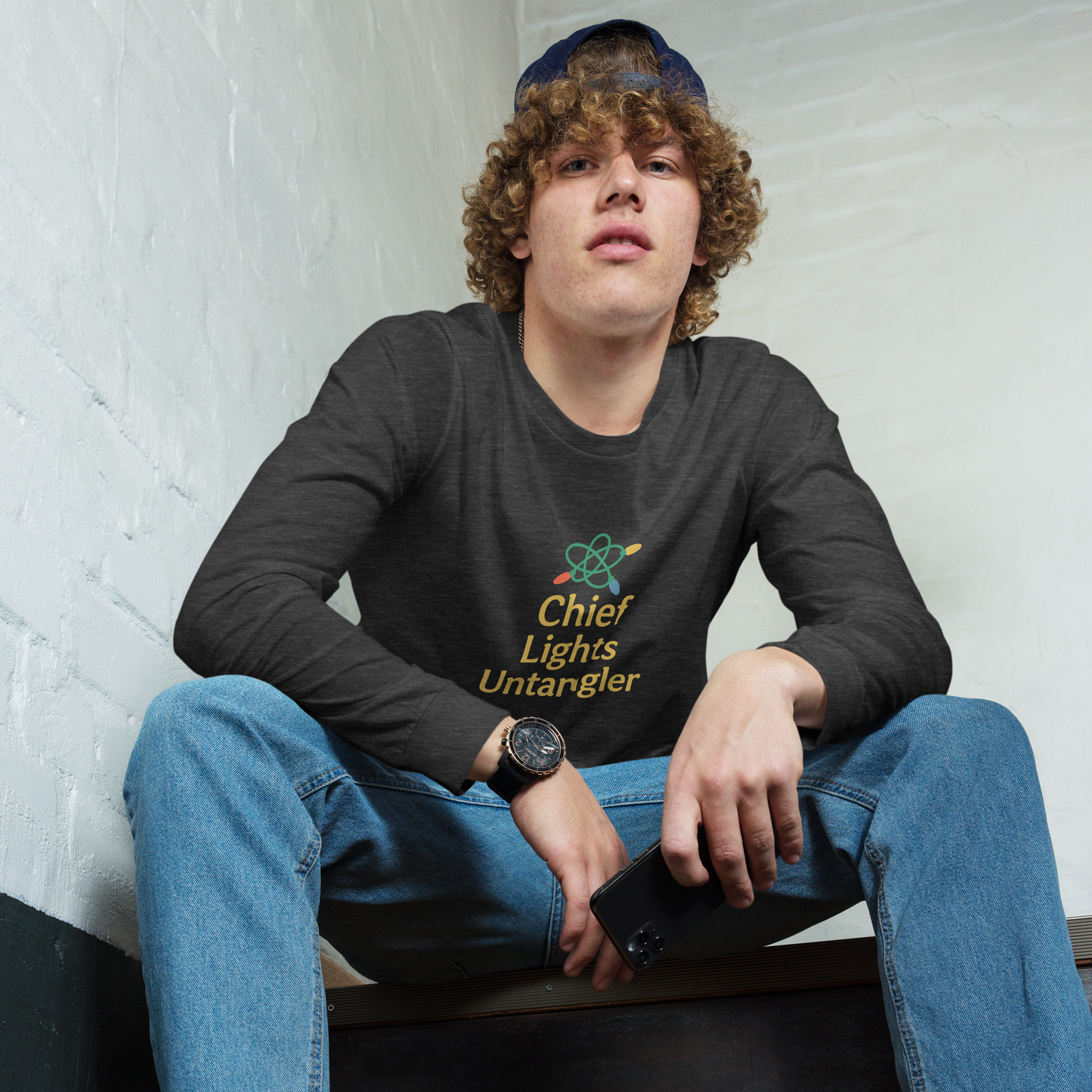 Person wearing a black long-sleeve shirt with text and graphics, sitting against a white brick wall.