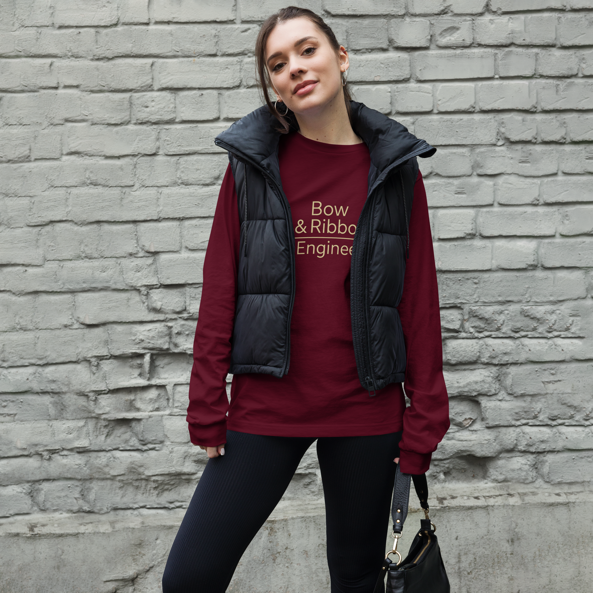 Woman wearing a red shirt with text and black vest against a brick wall