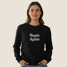 Woman wearing a black sweatshirt with "Begin Again" on the front.