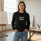 Woman in a studio wearing a black sweatshirt that says "Begin Again"