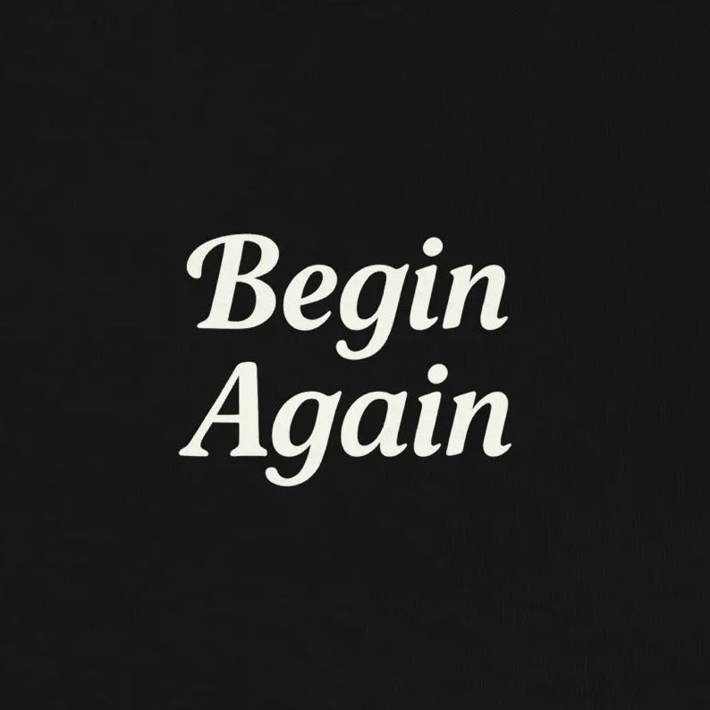 Black sweatshirt with 'Begin Again' text on a beige background
