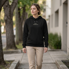 Person wearing a black hoodie with text, beige pants, and white shoes walking on a sidewalk.