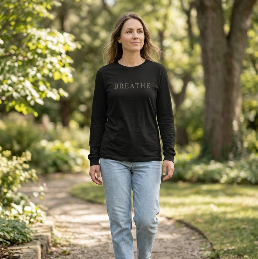 Woman wearing a black 'BREATHE' shirt walking on a path in a garden.