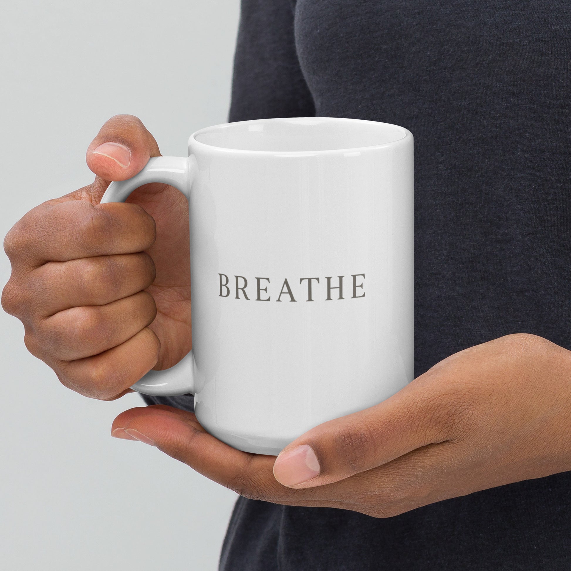 Person holding a white mug with 'BREATHE' text on a plain background