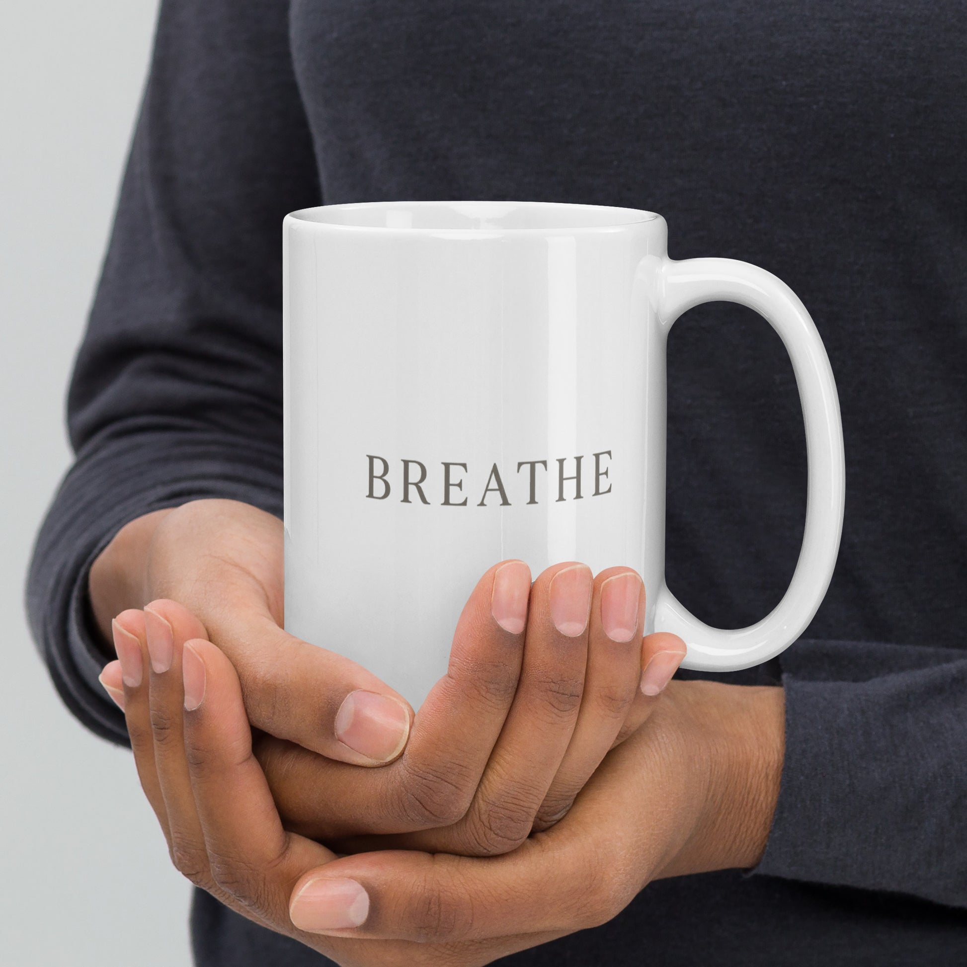 Person holding a white mug with 'BREATHE' text on a neutral background