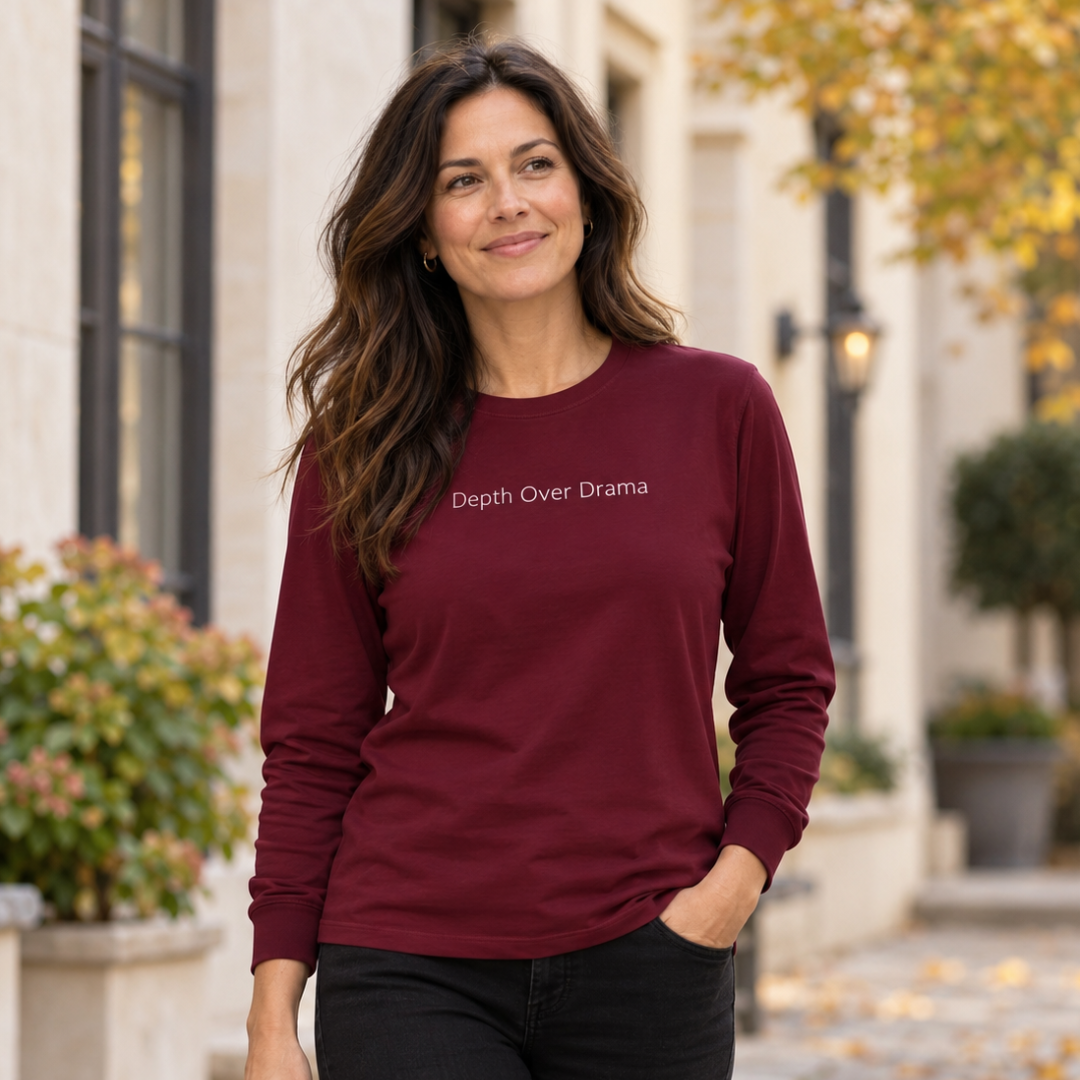 Woman walking down a street wearing a maroon long sleeve tee with Depth Over Drama on the upper chest and black jeans.