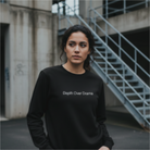 Woman wearing a black sweatshirt with 'Depth Over Drama' text in an urban setting