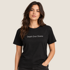 A woman modeling a black short-sleeve crewneck t-shirt with the phrase 'Depth Over Drama' printed in white across the chest, set against a solid light beige background.