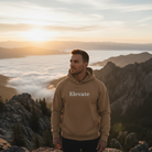 Man standing on top of a ridge wearing a khaki hoodie that says "Elevate"