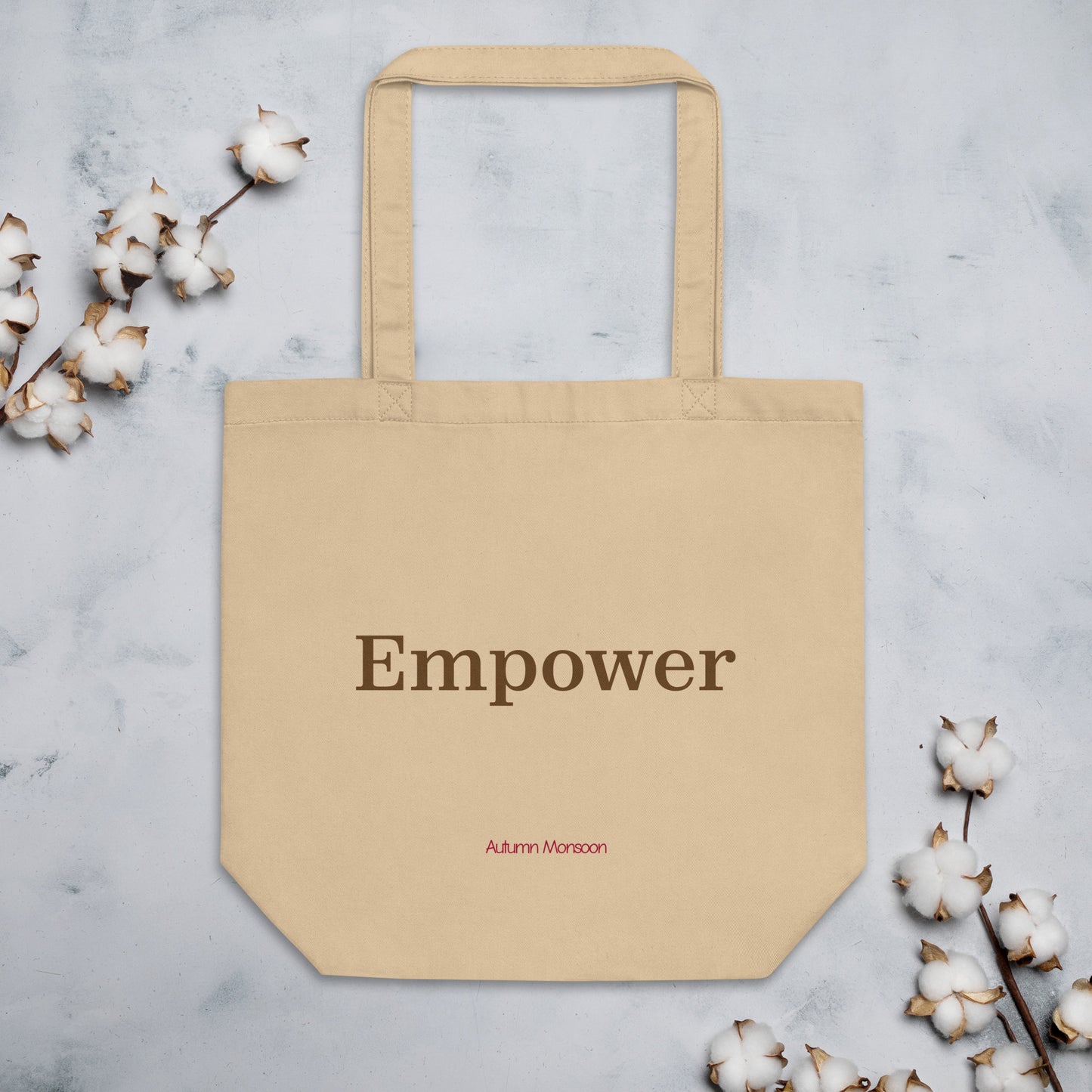Beige tote bag with 'Empower' text on a light gray background with cotton branches.