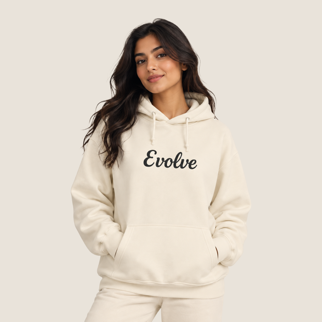 A woman wearing a cream-colored hoodie with the word 'Evolve' printed in black script across the chest, posed against a solid light beige background.