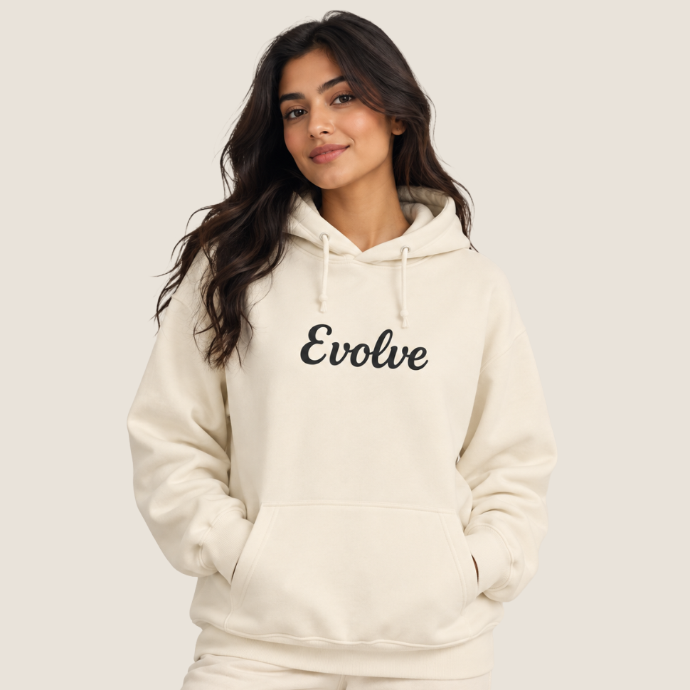 A woman wearing a cream-colored hoodie with the word 'Evolve' printed in black script across the chest, posed against a solid light beige background.