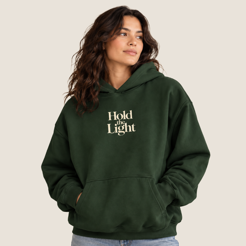 Woman wearing a forest green hoodie with Hold the Light on the center chest.