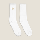 A pair of white ribbed crew socks on a light beige background, featuring a gold embroidered 'HAM' logo on the left sock's cuff.
