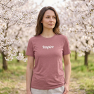 Woman wearing a pink t-shirt with 'Inspire' text, standing in a cherry blossom garden.
