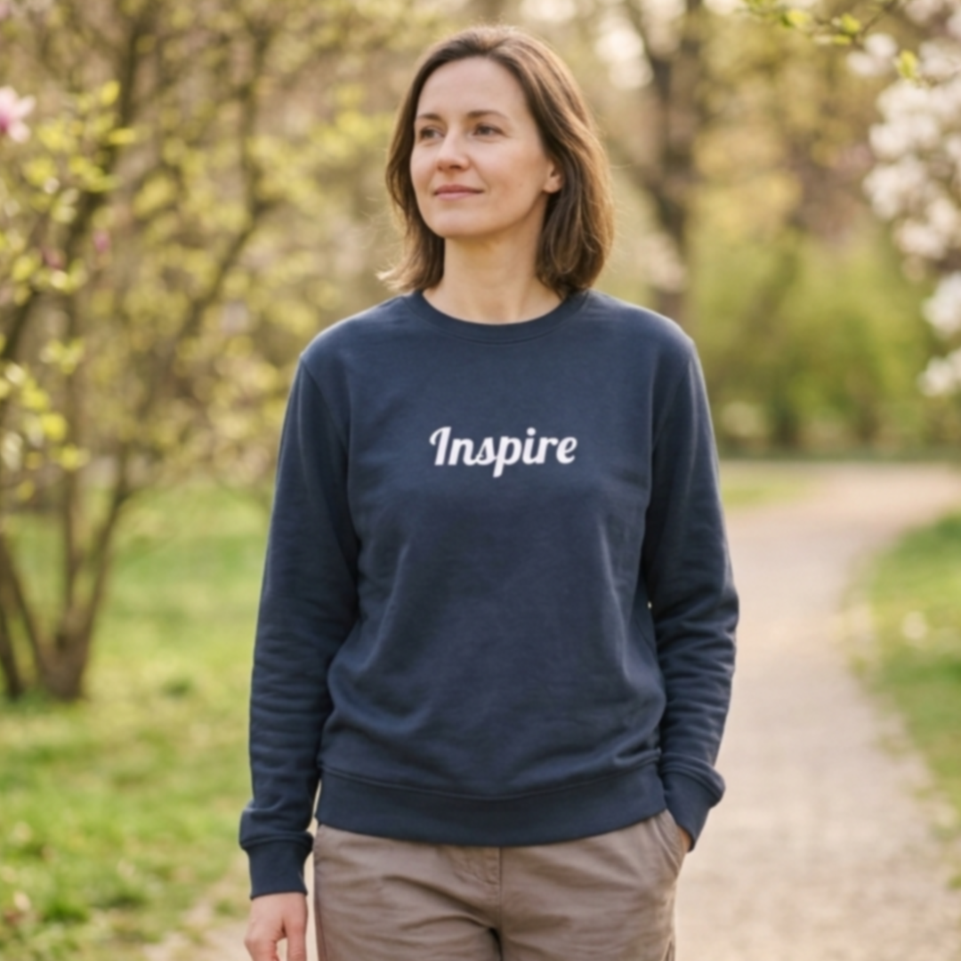 Women wearing a navy crewneck sweatshirt with the word "Inspire" across the chest. She is on a path in an outdoor setting with trees.