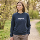 Women wearing a navy crewneck sweatshirt with the word "Inspire" across the chest. She is on a path in an outdoor setting with trees.