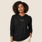 Woman wearing a black hooded long sleeve tee that says Intentional Living along with cream pants.