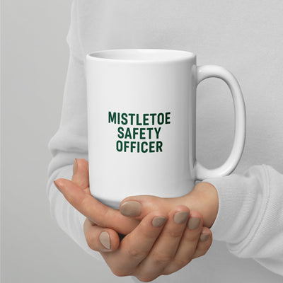 White mug with 'MISTLETOE SAFETY OFFICER' text held by a person against a light gray background
