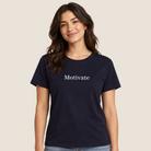 A woman modeling a navy blue short-sleeve t-shirt with the word 'Motivate' printed in white serif font across the chest, paired with light-wash blue jeans against a solid light beige background.