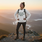 Person standing on a mountain with a scenic view during sunset, wearing a white sweatshirt with text.