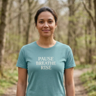 Woman wearing a teal t-shirt with 'PAUSE BREATHE RISE' text in a forest setting