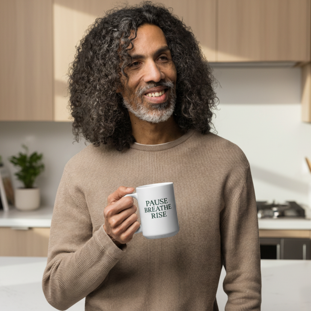 Man holding a mug with 'Pause, Breathe, Rise' text in a kitchen setting