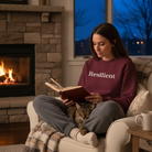 Woman reading a book with a cat on her lap in a cozy living room with a fireplace.
