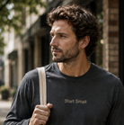 Man in grey Start Small long sleeve tee walk-in down a street holding a tote bag over his shoulder.