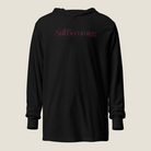 A black long-sleeve hooded sweatshirt with the word 'Still Becoming' printed in a dark red serif font across the chest, displayed against a solid light beige background.