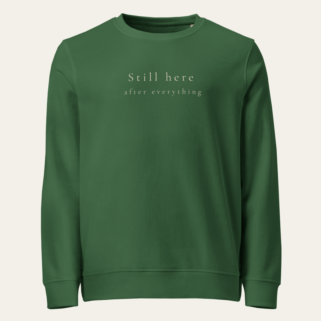 Bottle green crewneck sweatshirt with Still here after everything on upper center chest.