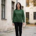 Woman wearing a Still Here crewneck sweatshirt walking down a stone street with stucco buildings in the background.