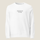 A white crewneck sweatshirt with 'Intentional Living' printed in black serif text on the chest, displayed against a solid light beige background.