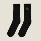A pair of black crew socks with the brand name 'HAM' embroidered in gold on the upper calf, displayed against a solid white background.