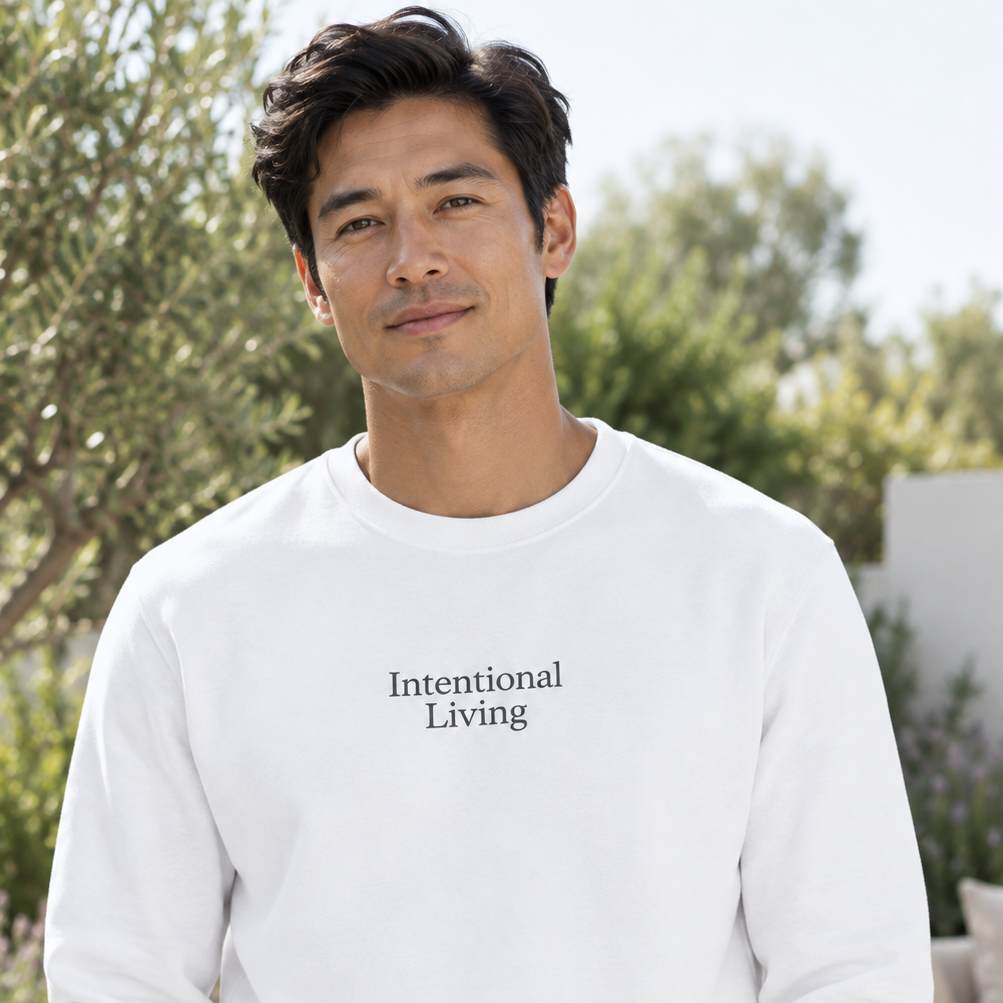 A man wearing a white crewneck sweatshirt with the text 'Intentional Living' printed in black on the chest, set against an outdoor patio background.