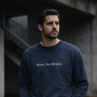 Man wearing a navy blue sweatshirt with 'Worn, Not Broken' text in an urban setting.