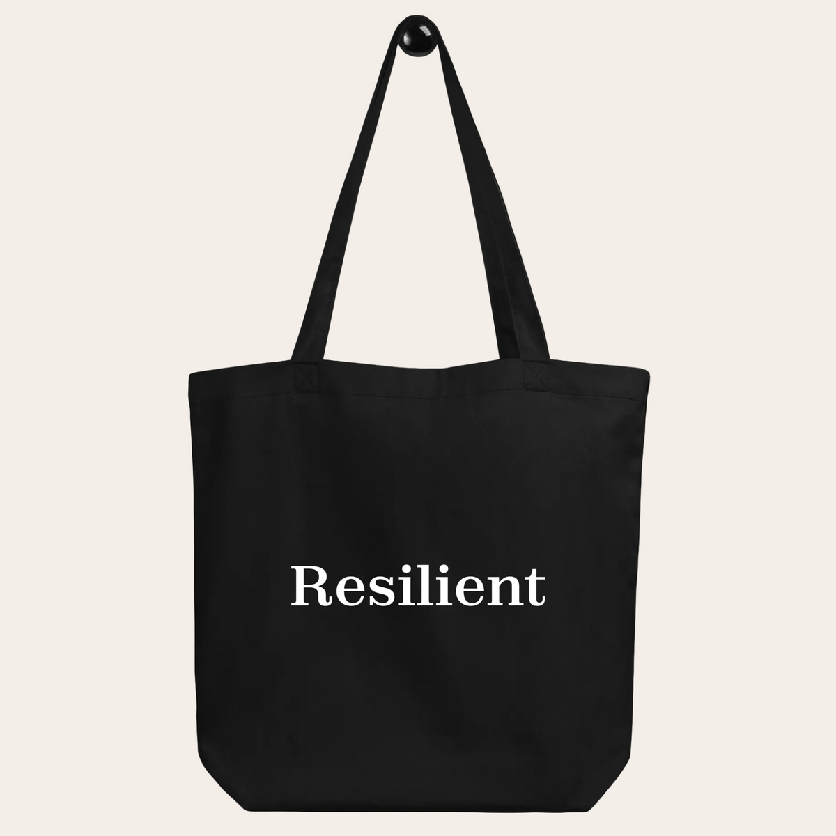 Black tote bag with 'Resilient' text on a beige background
